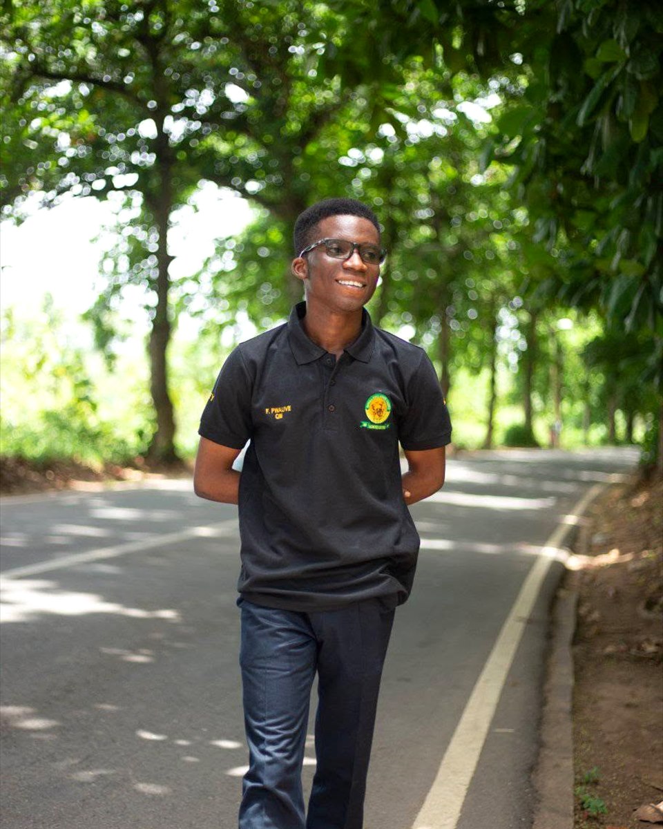 Francis Pwavwe walking along a tree-lined campus road